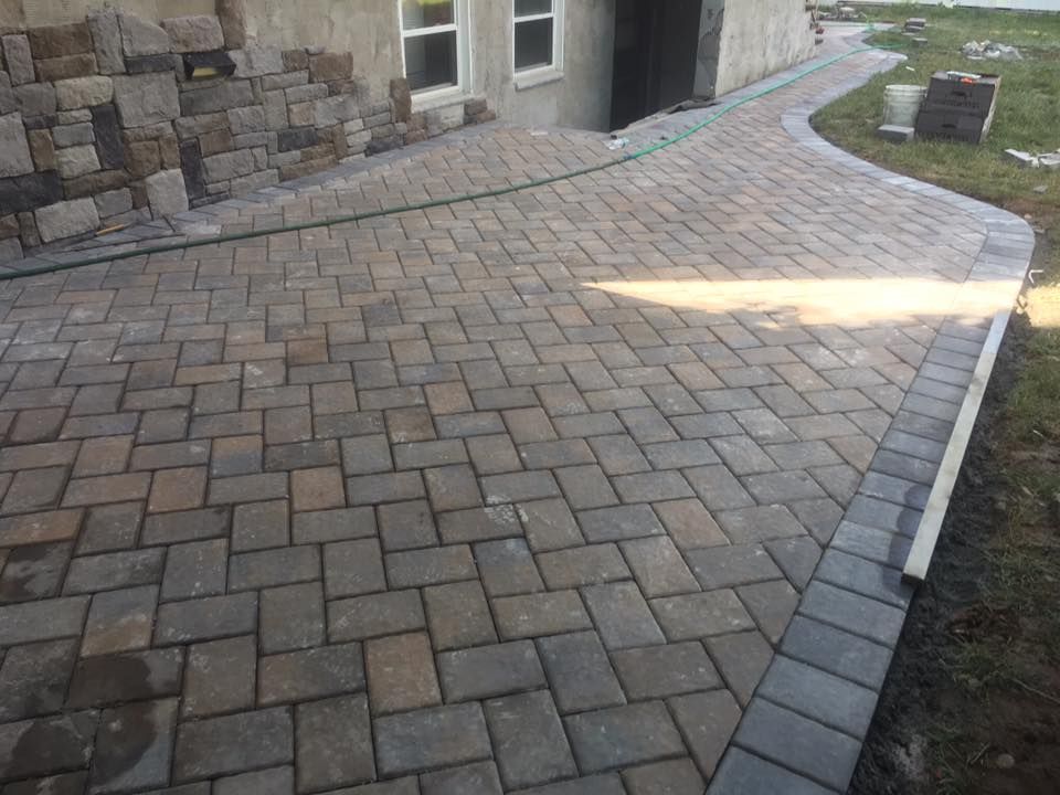 Bricklayer using a hammer to fit a brick into a wall, with blueprints and a yellow hard hat.