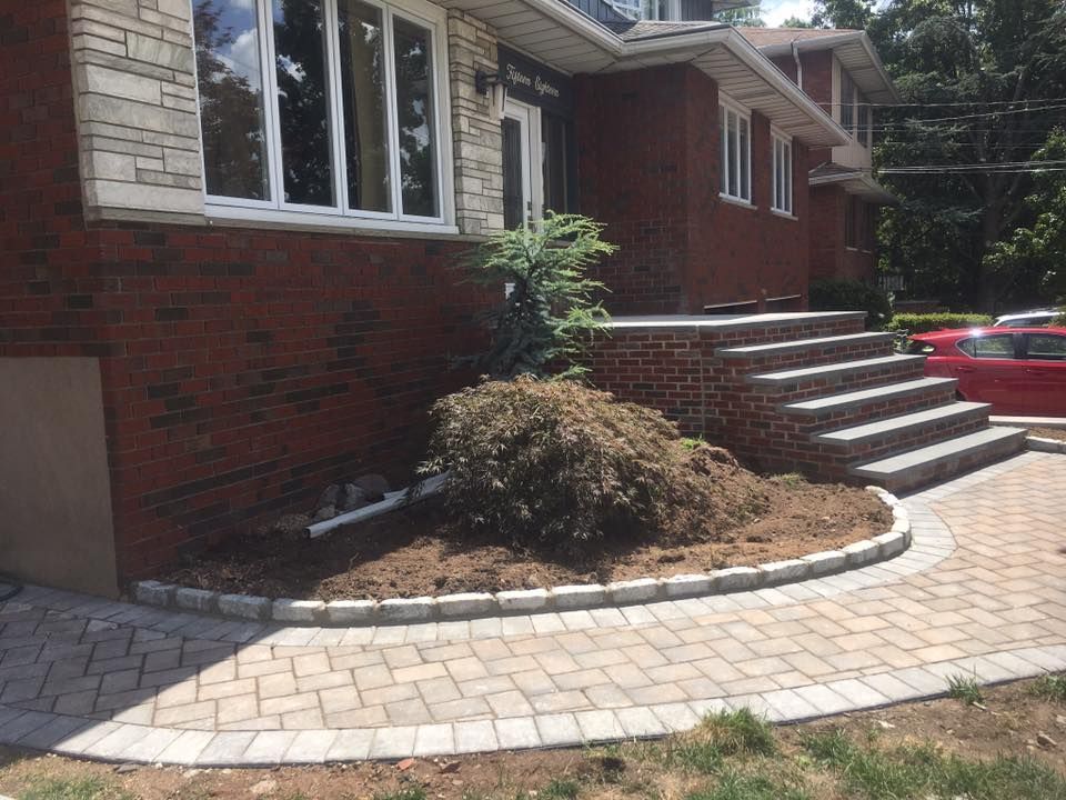 Person in orange gloves uses a yellow mallet to set pavers on a sand base.