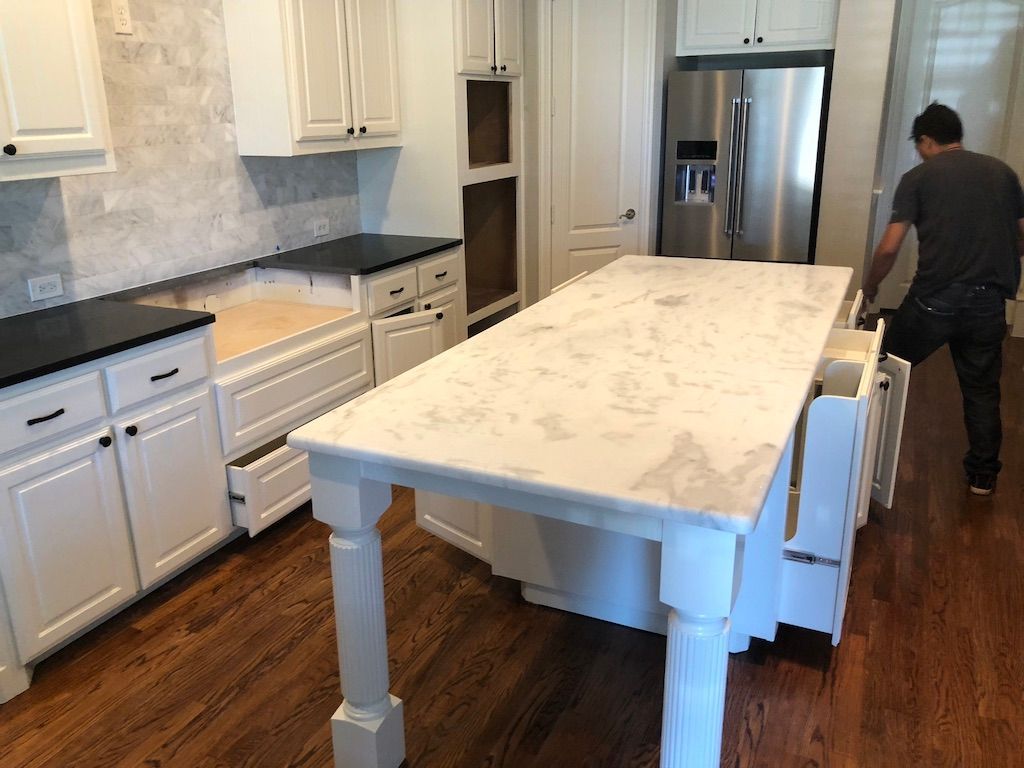 A person in a kitchen with white cabinets and a large island with a marble countertop.