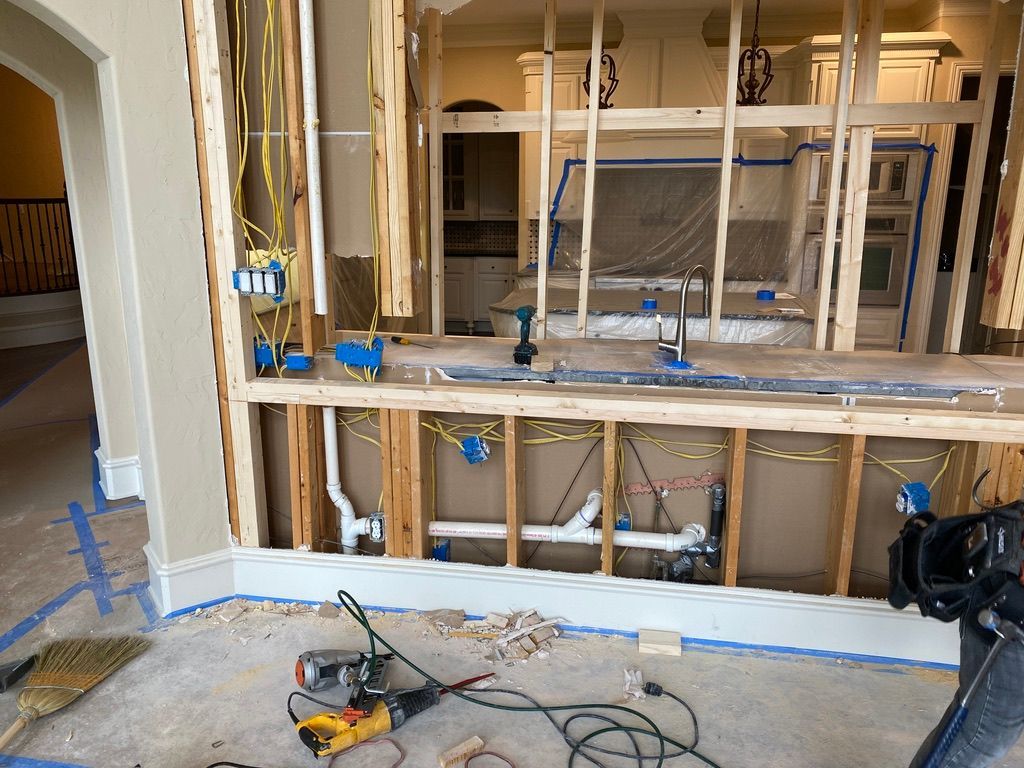Kitchen renovation in progress, showing exposed studs, electrical wiring, plumbing, and construction tools. Interior view.