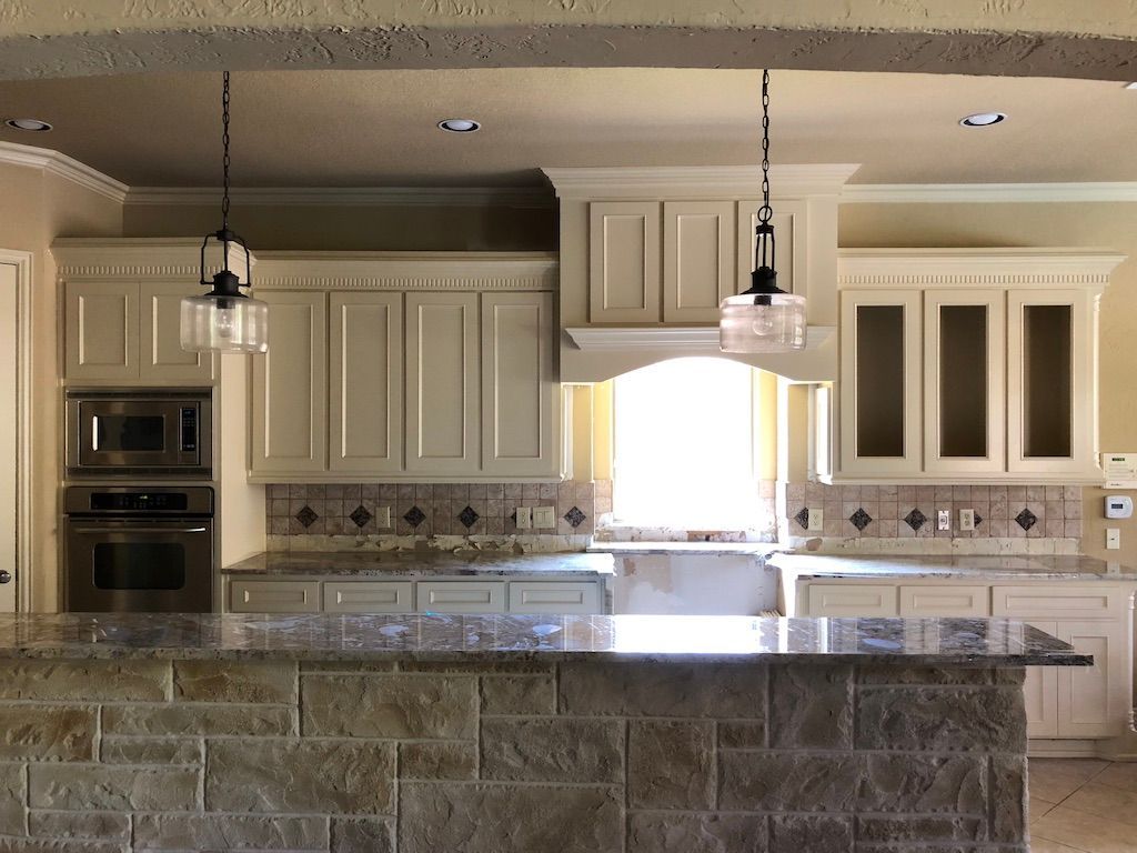 Kitchen with off-white cabinets, granite countertops, and a stone-faced island. Two pendant lights hang above the island.