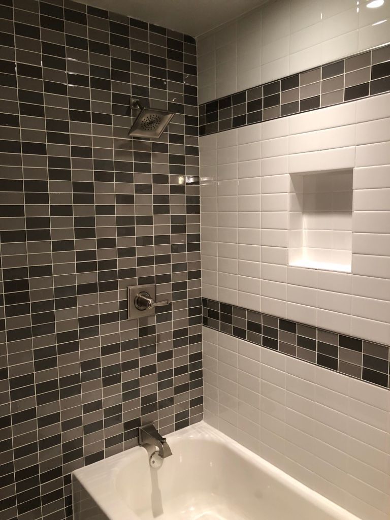 Bathroom with tiled walls. Shower area features a mix of gray and white mosaic tiles. A built-in shelf is visible.