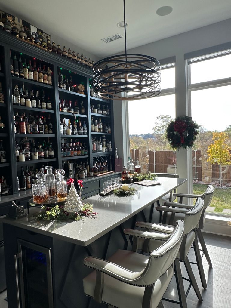 A home bar with a large wall of liquor bottles, a counter with bar stools, and a window with an outdoor view.