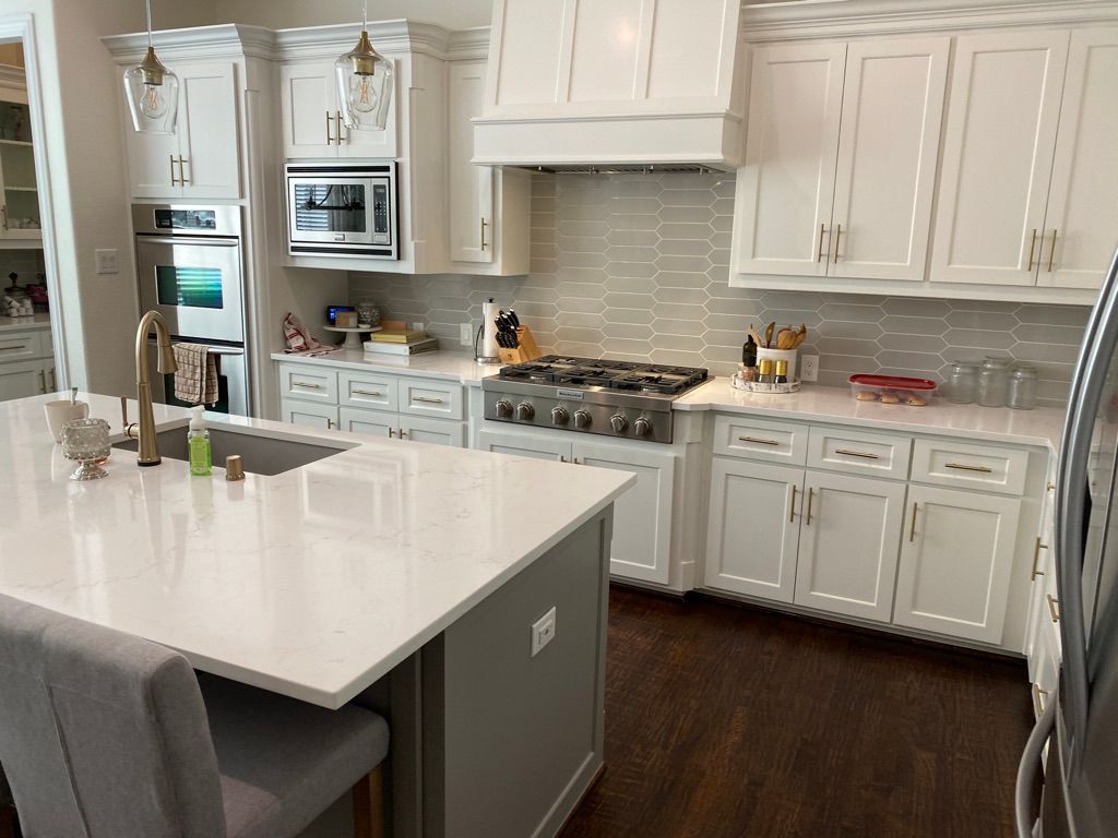 White kitchen with island, stainless steel appliances, and gray countertop. The room has white cabinetry and dark wood floors.