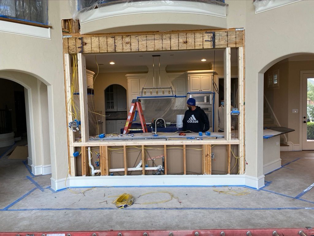 Interior view showing a window frame under construction, with a person working inside and a kitchen visible in the background.