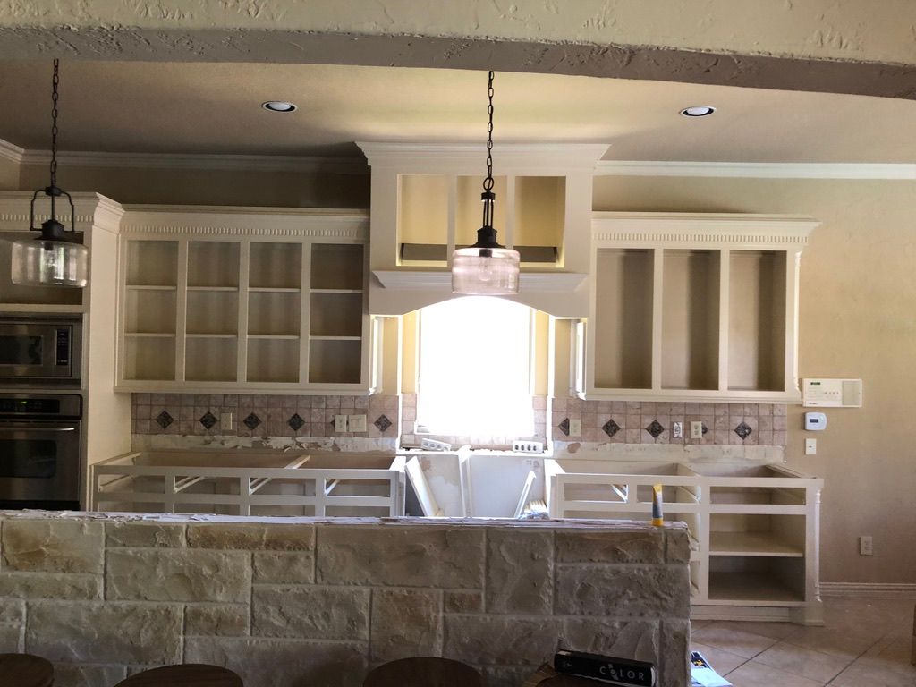 Kitchen remodel in progress: Light cabinets with open shelving, stone island, exposed countertops, and hanging pendant lights.