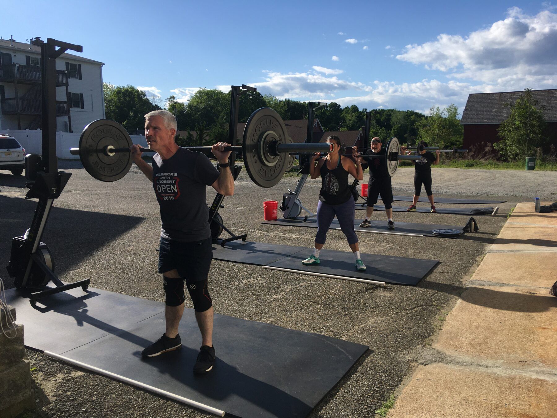 A man is squatting with a barbell in a parking lot