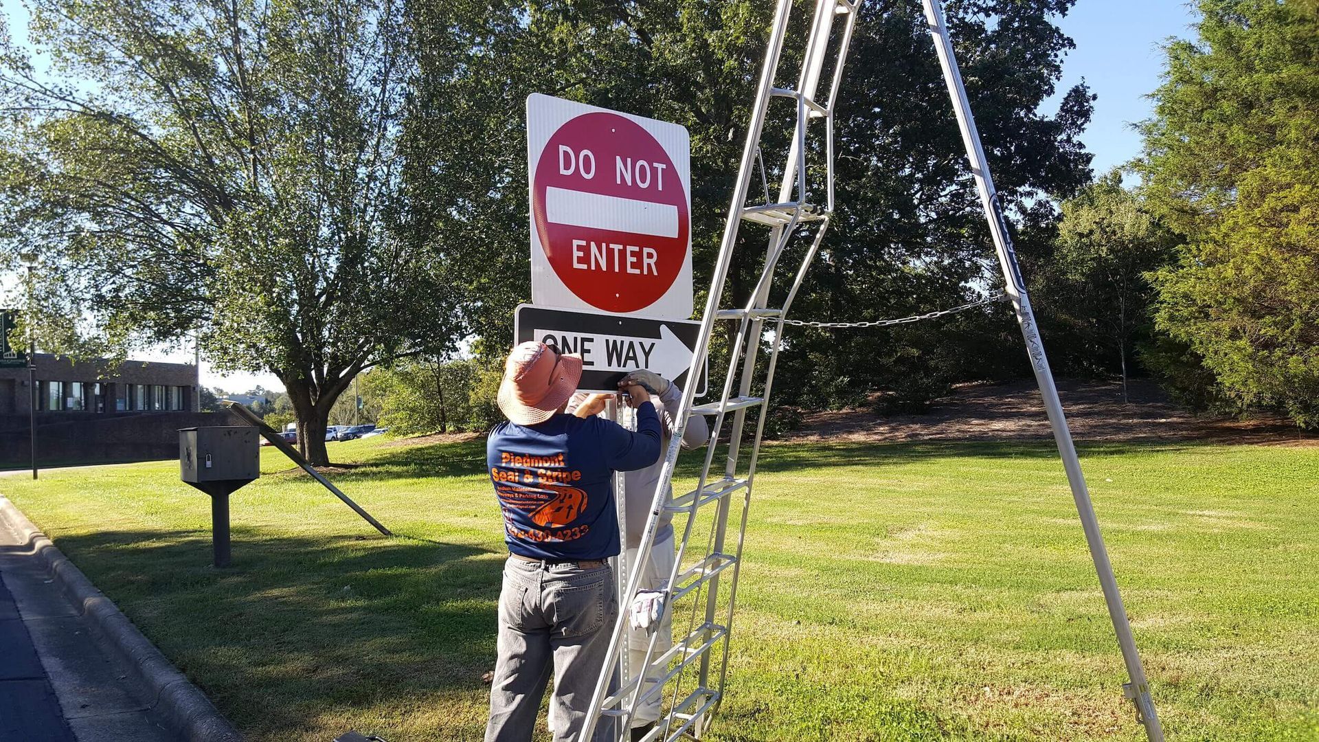 A man is standing on a ladder fixing a do not enter sign.