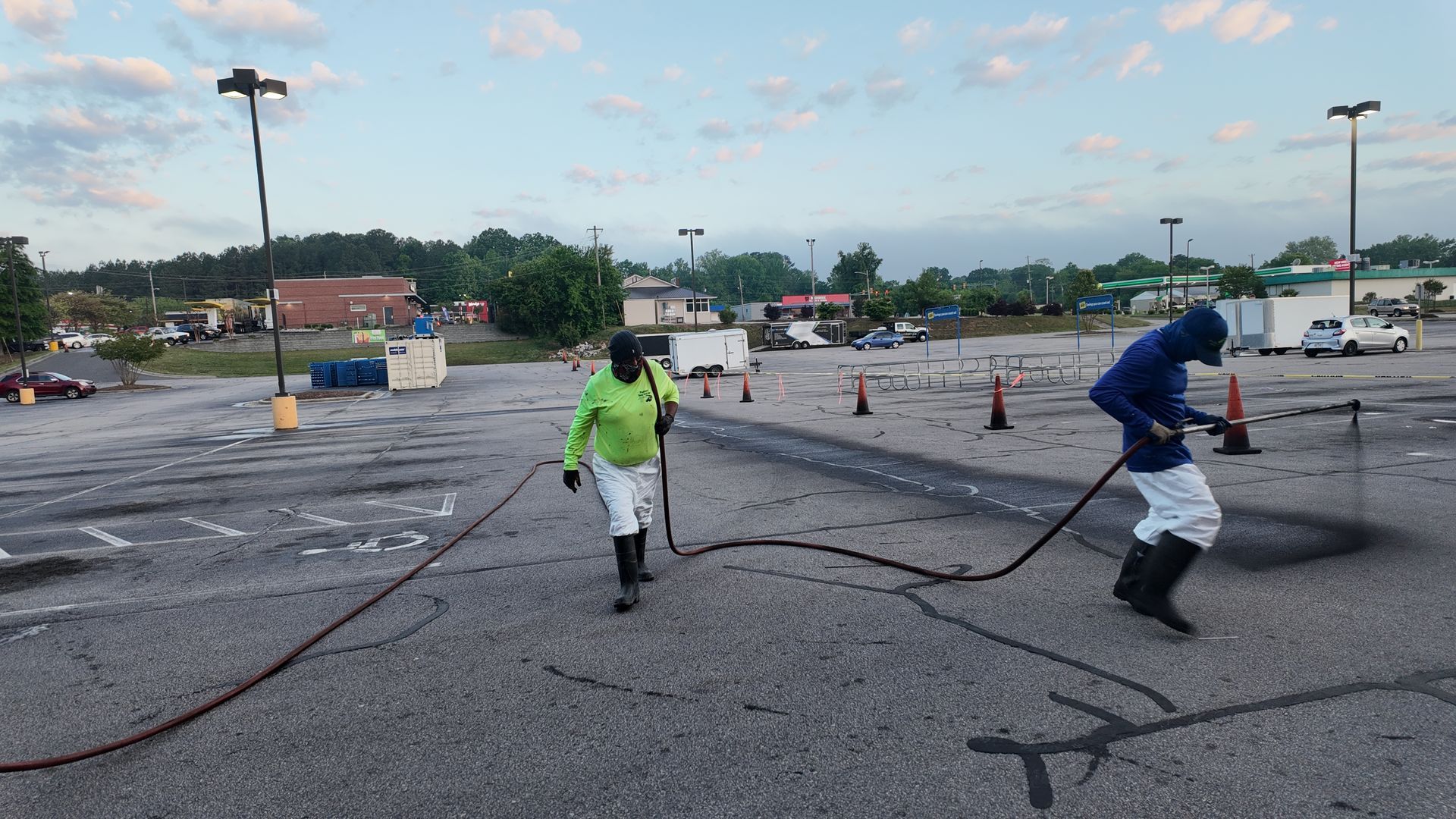 Two men are working on a parking lot with a hose.