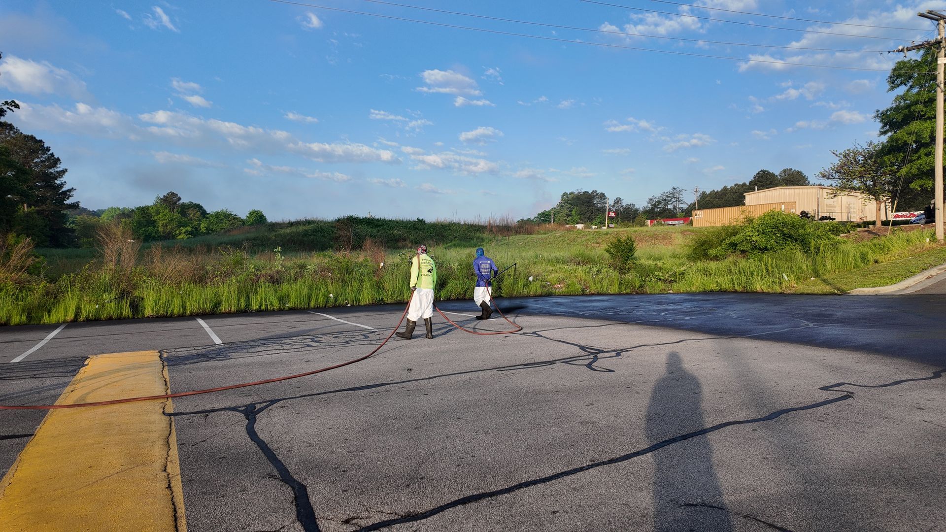 Two men are standing in a parking lot spraying asphalt.