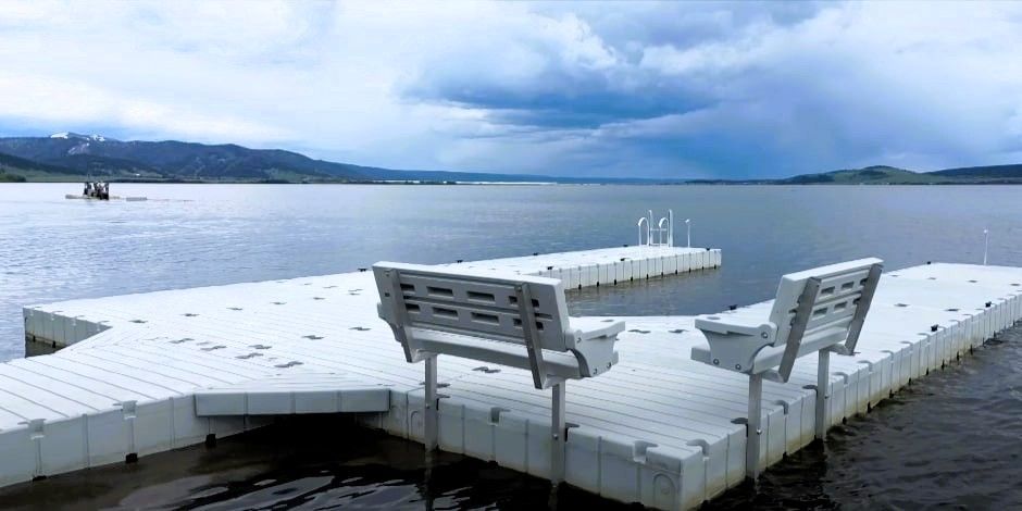 White benches on a floating dock with a cloudy sky over a mountain lake.