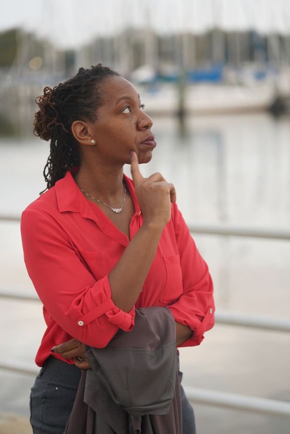 A woman in a red shirt is standing in front of a body of water.