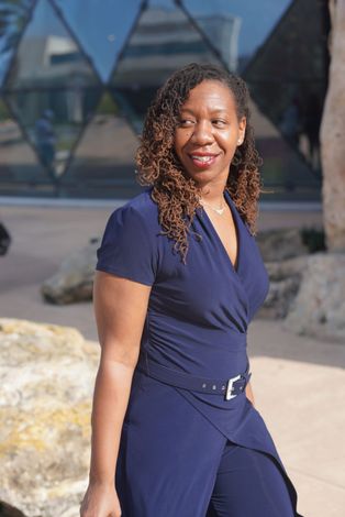 A woman in a blue dress is standing in front of a building.