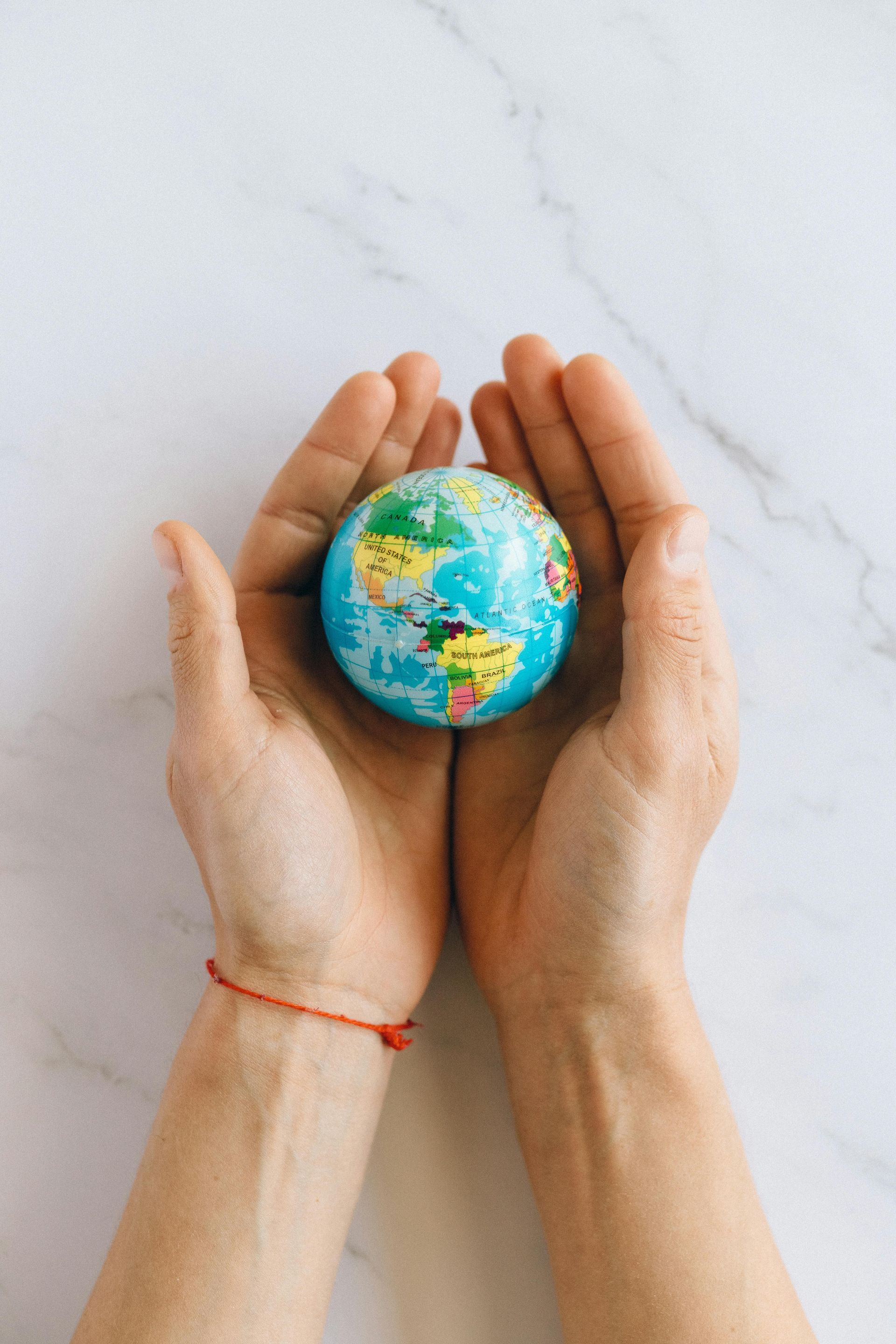 Hands cradling a small globe, emphasizing worldwide services offered. The background is a white marble surface.