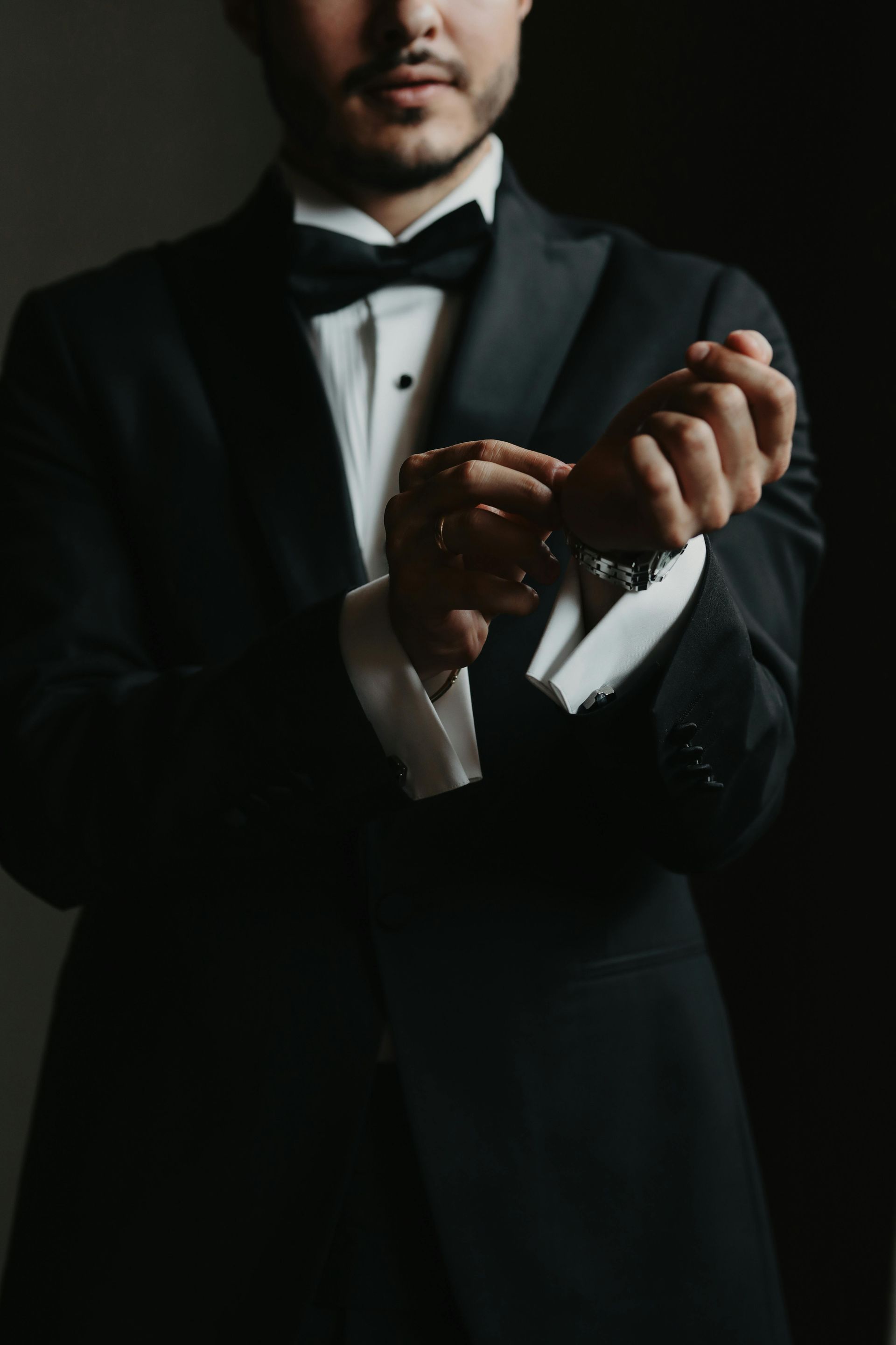 Man in black tuxedo adjusting cufflink.