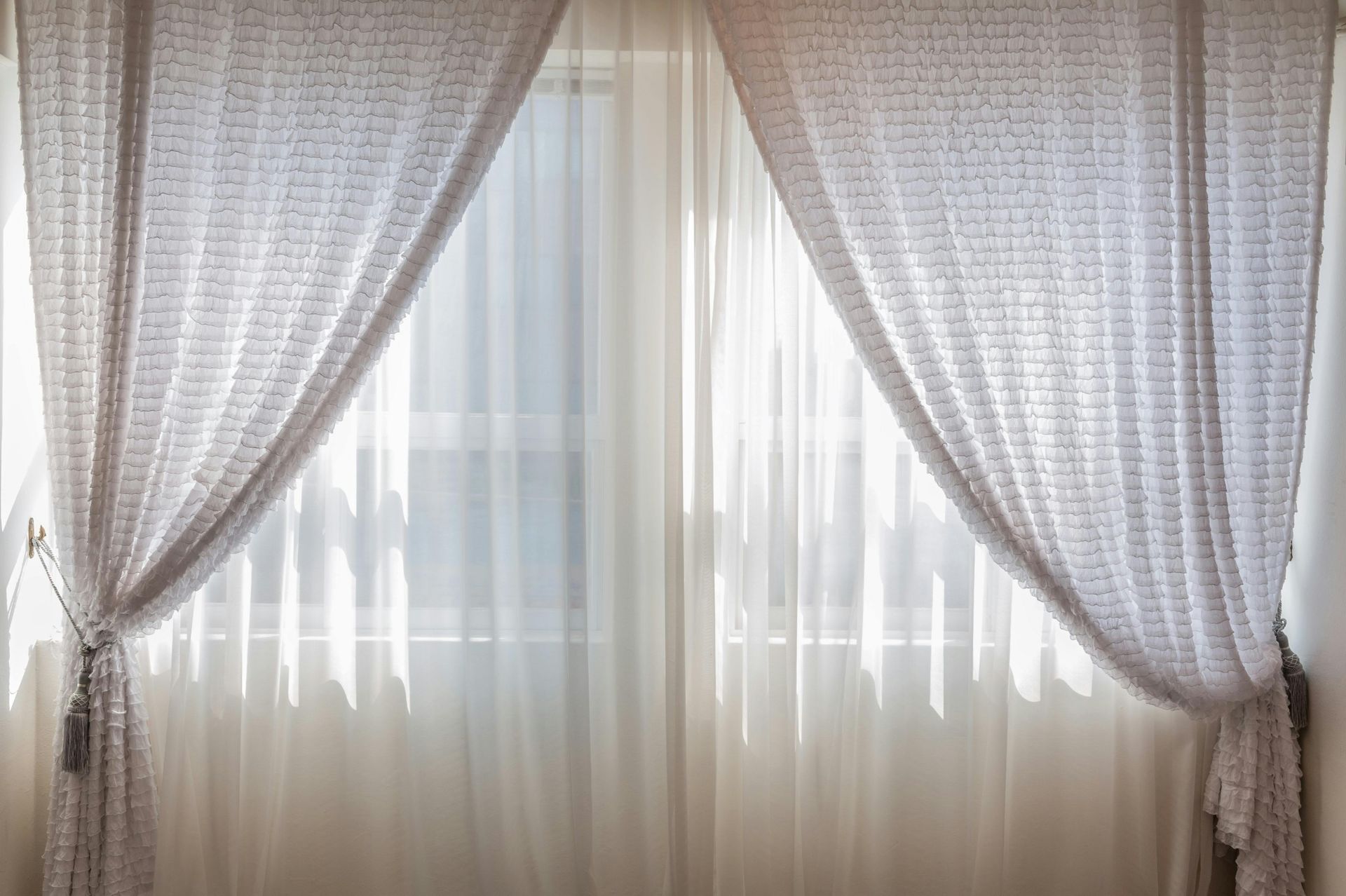 White sheer curtains draped across a window, letting in sunlight.