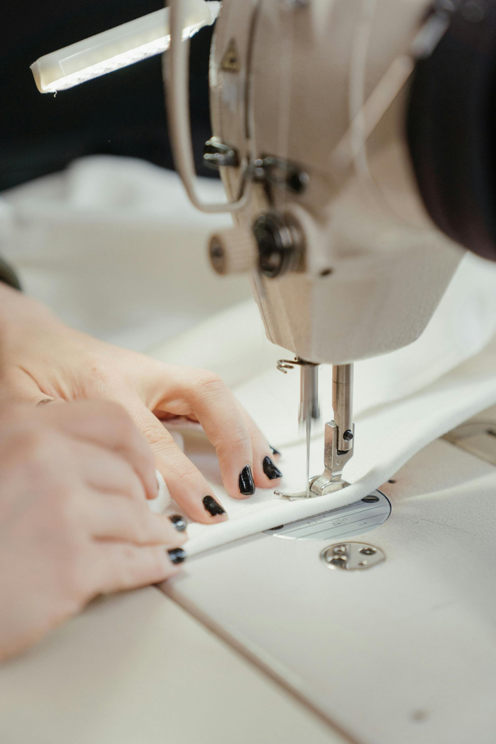 Hands using a white sewing machine to stitch white fabric.