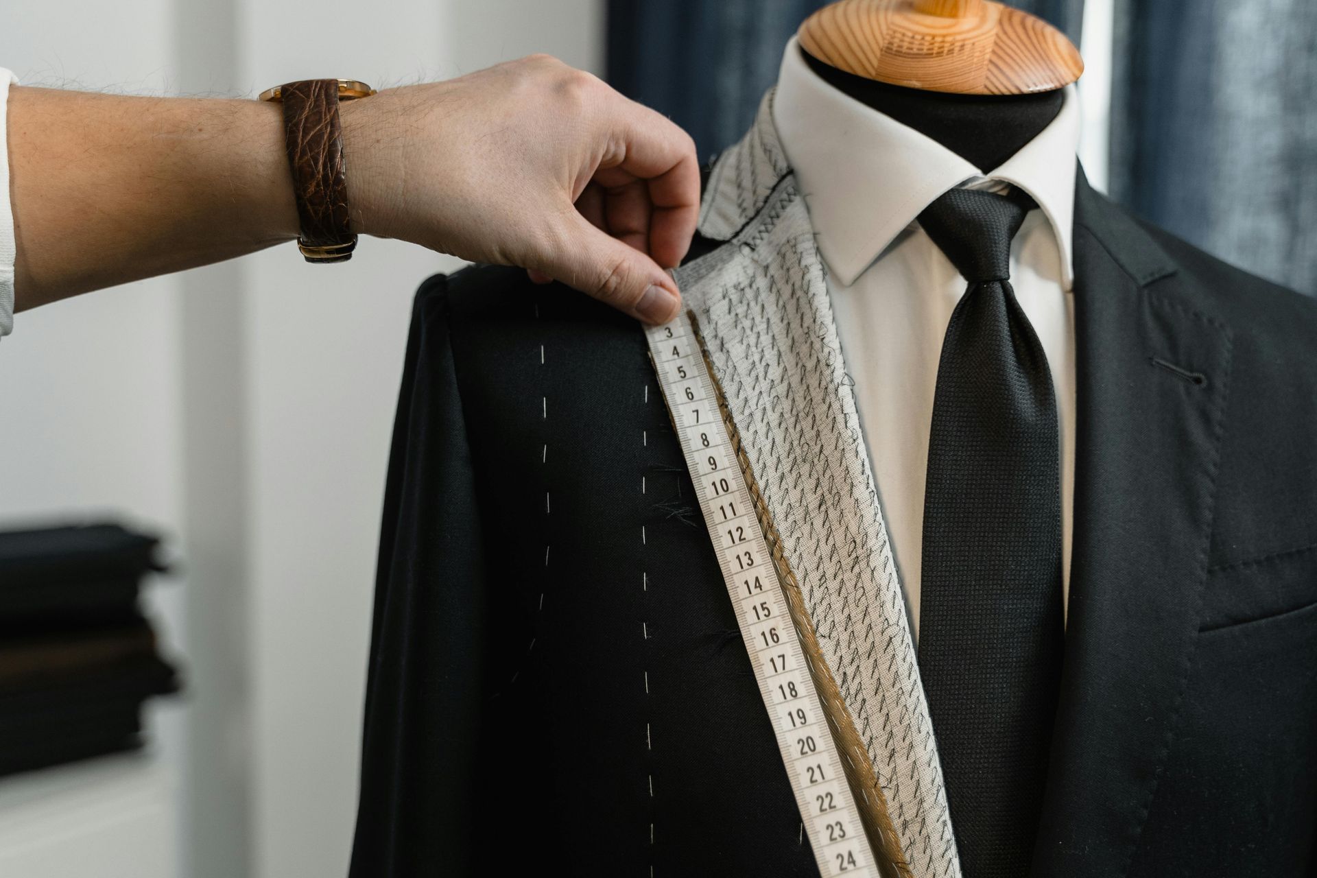 Tailor measuring the shoulder of a dark suit on a mannequin.