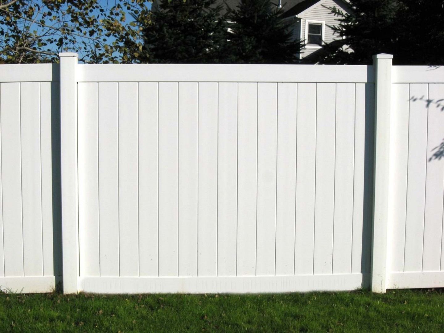 White vinyl fence in a grassy yard, with a house visible in the background.