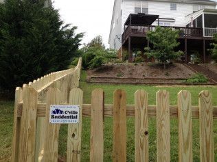 Wooden picket fence in a yard with a house on a small hill in the background.