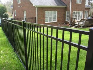 Black metal fence surrounding a green lawn in front of a brick house.