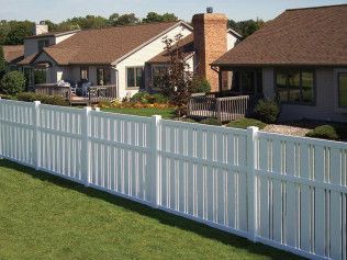 White vinyl fence in front of suburban houses with brown roofs and a green lawn.