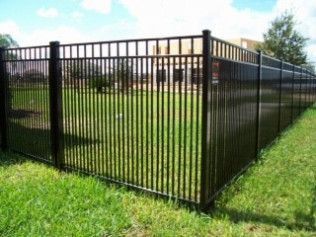 Black metal fence on green grass, surrounding a yard.