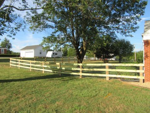 A wooden fence surrounds a grassy yard with a tree, a white garage, and a brick building.