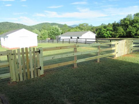 Wooden fence with gate in front of two white buildings and green hills.