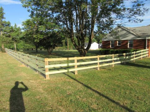 Wooden fence in a grassy yard, with a house and trees in the background. A shadow is in the foreground.