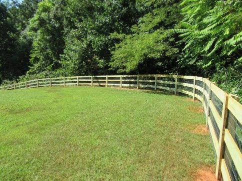 Green lawn enclosed by a wooden fence, with trees in the background under a sunny sky.