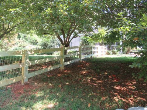 Wooden fence in a grassy yard, under shade of trees, with a house in the background.