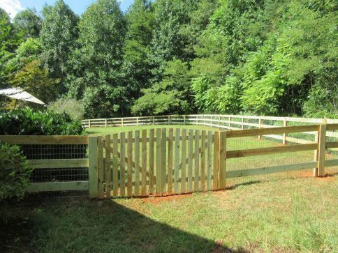 Wooden gate and fence in a grassy yard, with trees in the background.