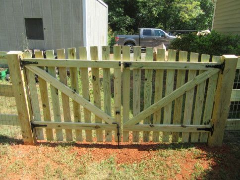 Wooden double gate with diagonal braces in a yard, connected to a wooden fence.
