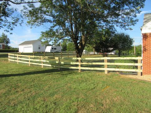 Wooden fence enclosing a grassy yard with a house, tree, and garage in the background on a sunny day.