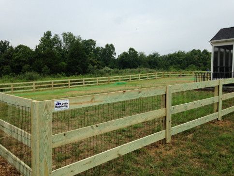 Wooden fence with wire mesh in a grassy yard, trees in the background.