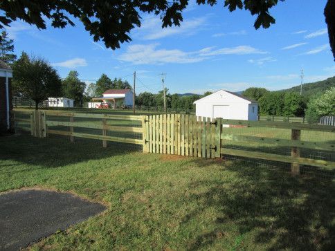 Wooden fence with gate in front yard, white barn in background, sunny day.