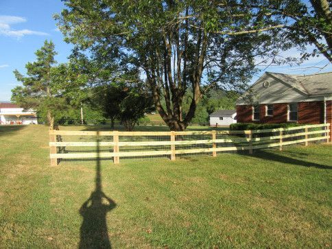Wooden fence in a grassy yard, with a tree, a house, and a person's shadow.