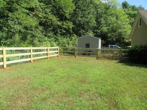 A freshly built wooden fence encloses a green lawn, shed and part of a house.