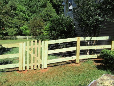 Wooden fence with a gate, in a grassy yard, with wire mesh, trees in the background.