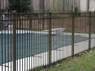 Brown metal fence surrounding a pool covered by a green tarp, in a backyard setting.