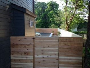 Wooden fence partially obscures a backyard with a building, trees, and glimpses of a pool.