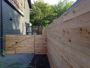 Wooden fence and gate next to a house with trees in the background.