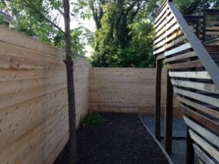 Wooden privacy fence surrounds a small backyard with a tree and a slatted structure.