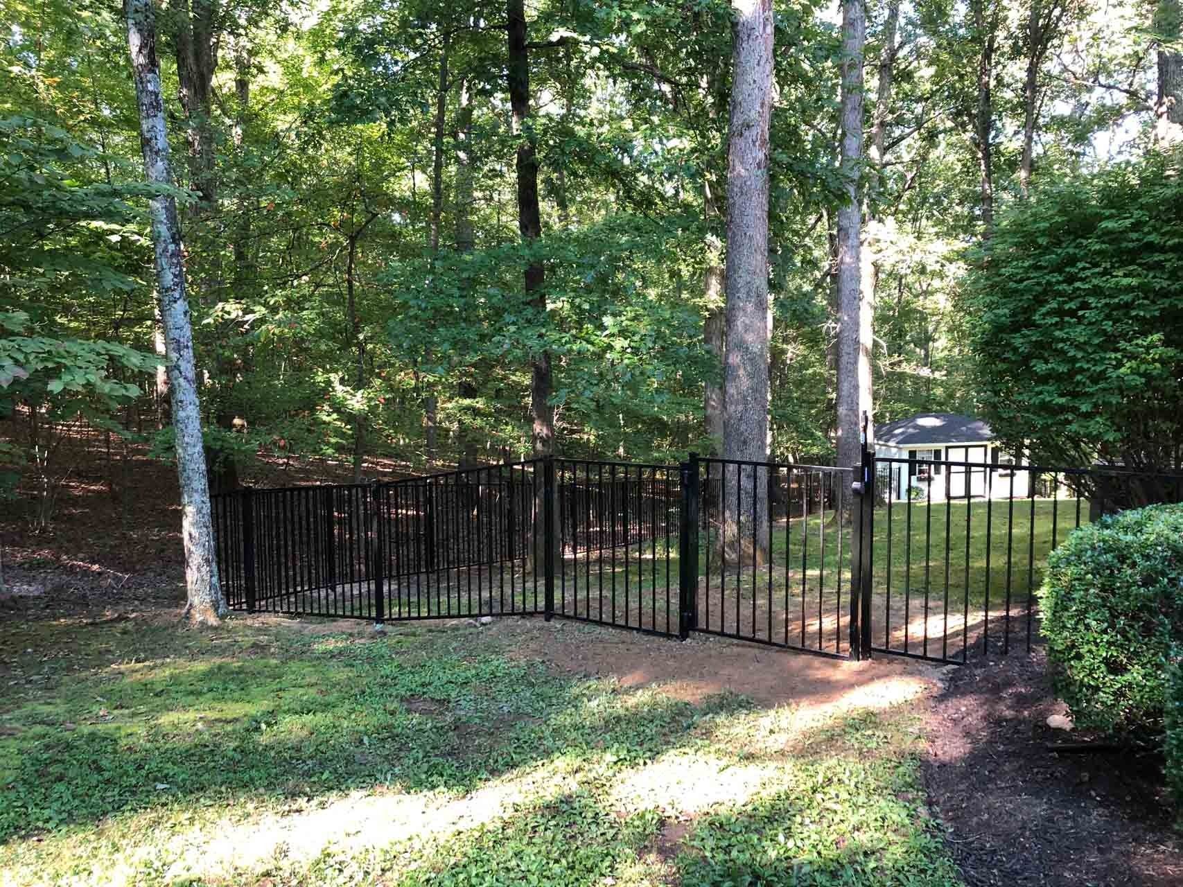 Black metal fence encloses a backyard with trees and a glimpse of a house.