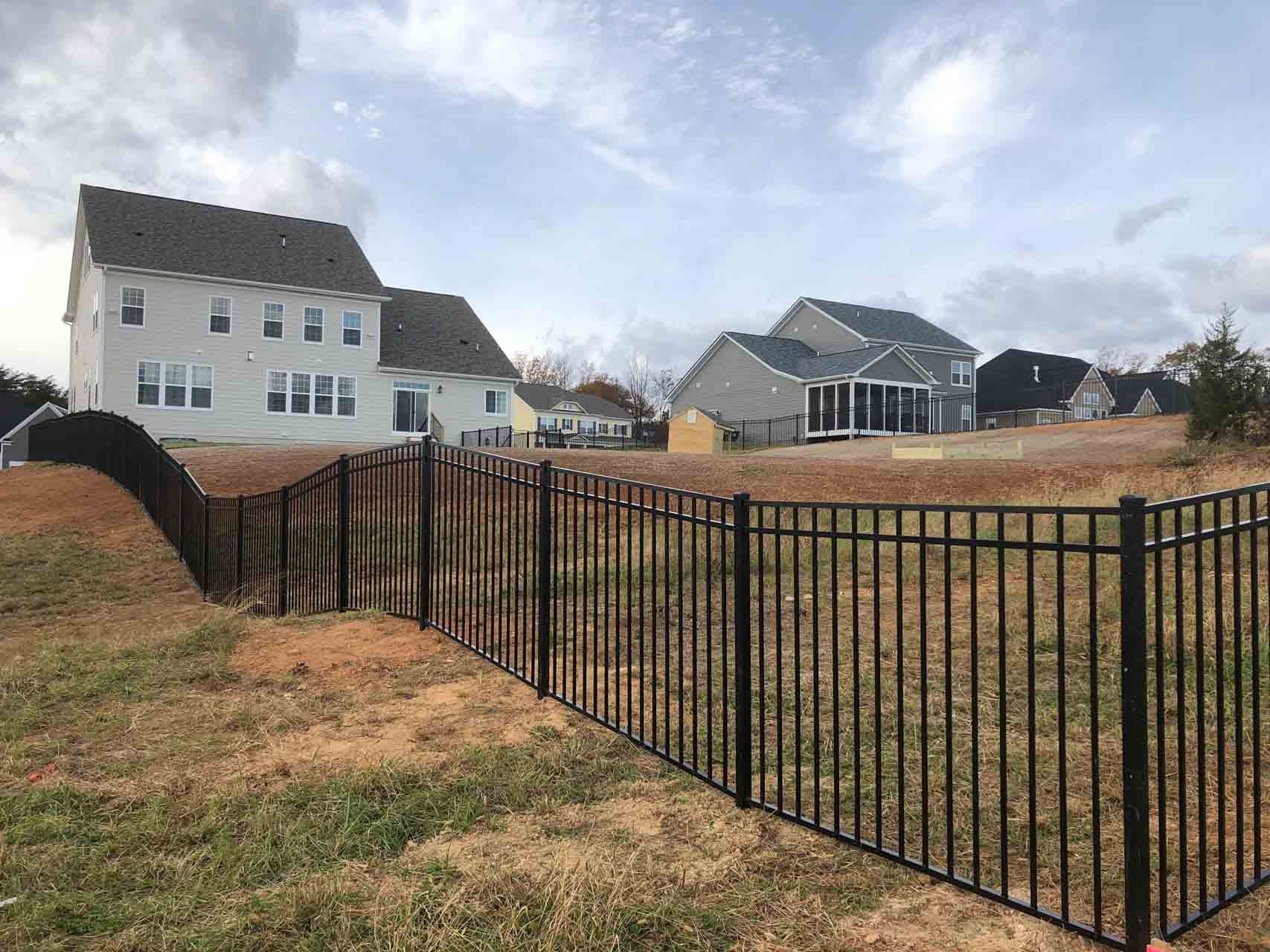Black metal fence bordering a dry grassy drainage area in a suburban neighborhood.