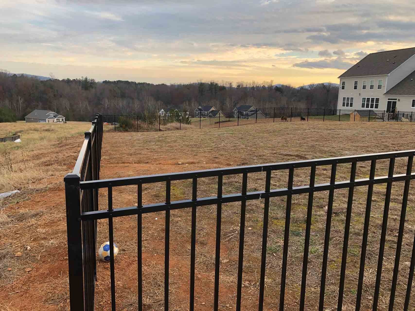 Black metal fence in front of a yard with a soccer ball and a house on a cloudy day.