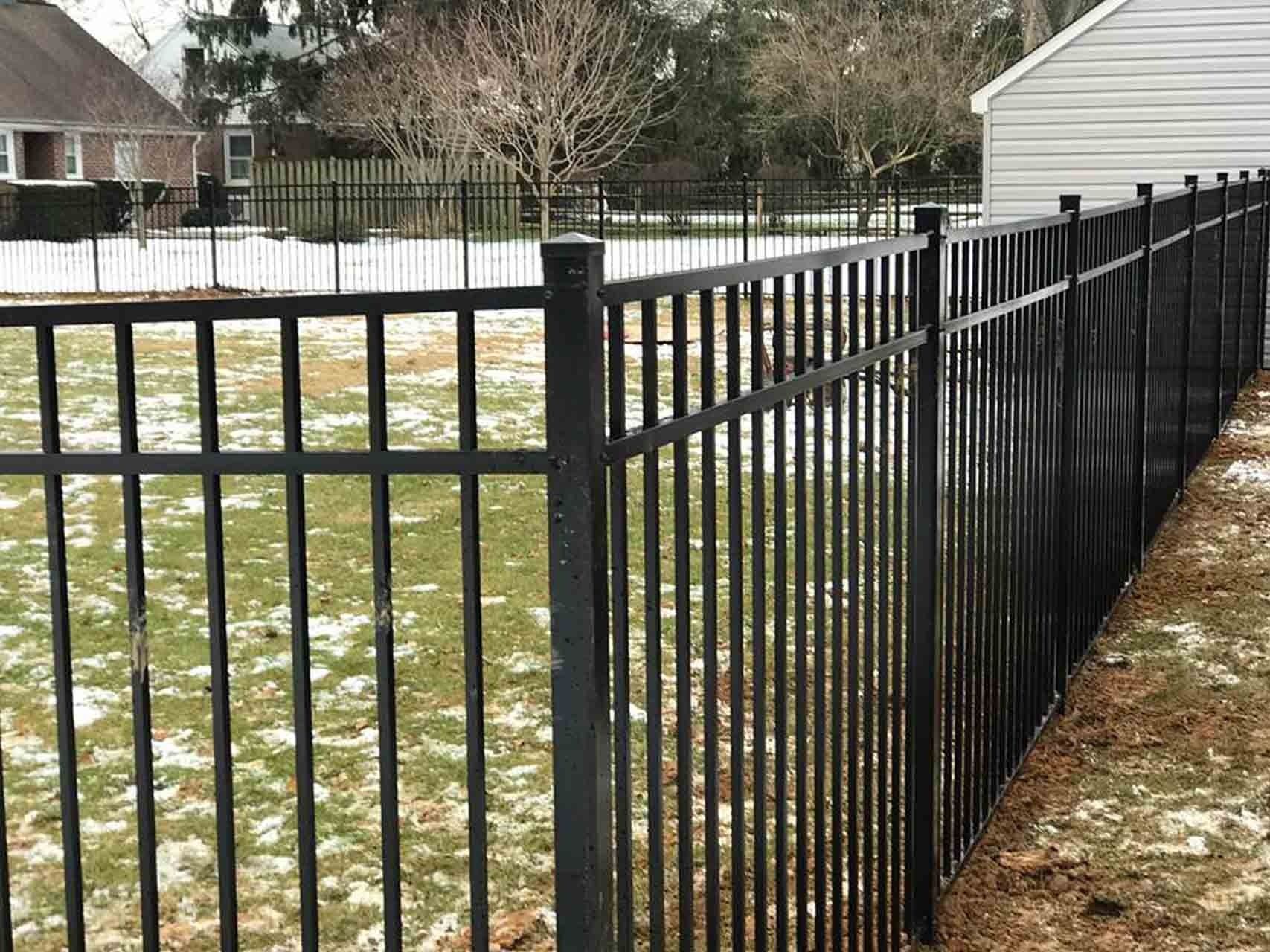 Black metal fence in a yard with some snow on the ground.