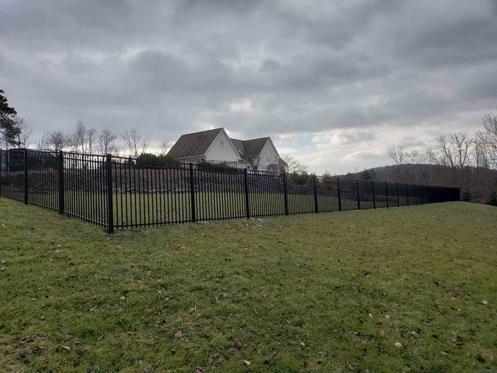 Black fence surrounds a grassy yard, with a two-story house under a cloudy sky in the background.
