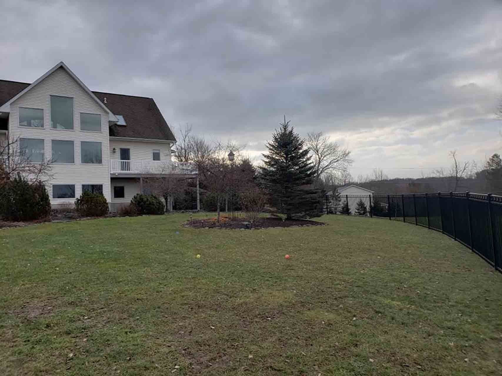 White house with lawn, evergreen tree, and black fence under a cloudy sky.